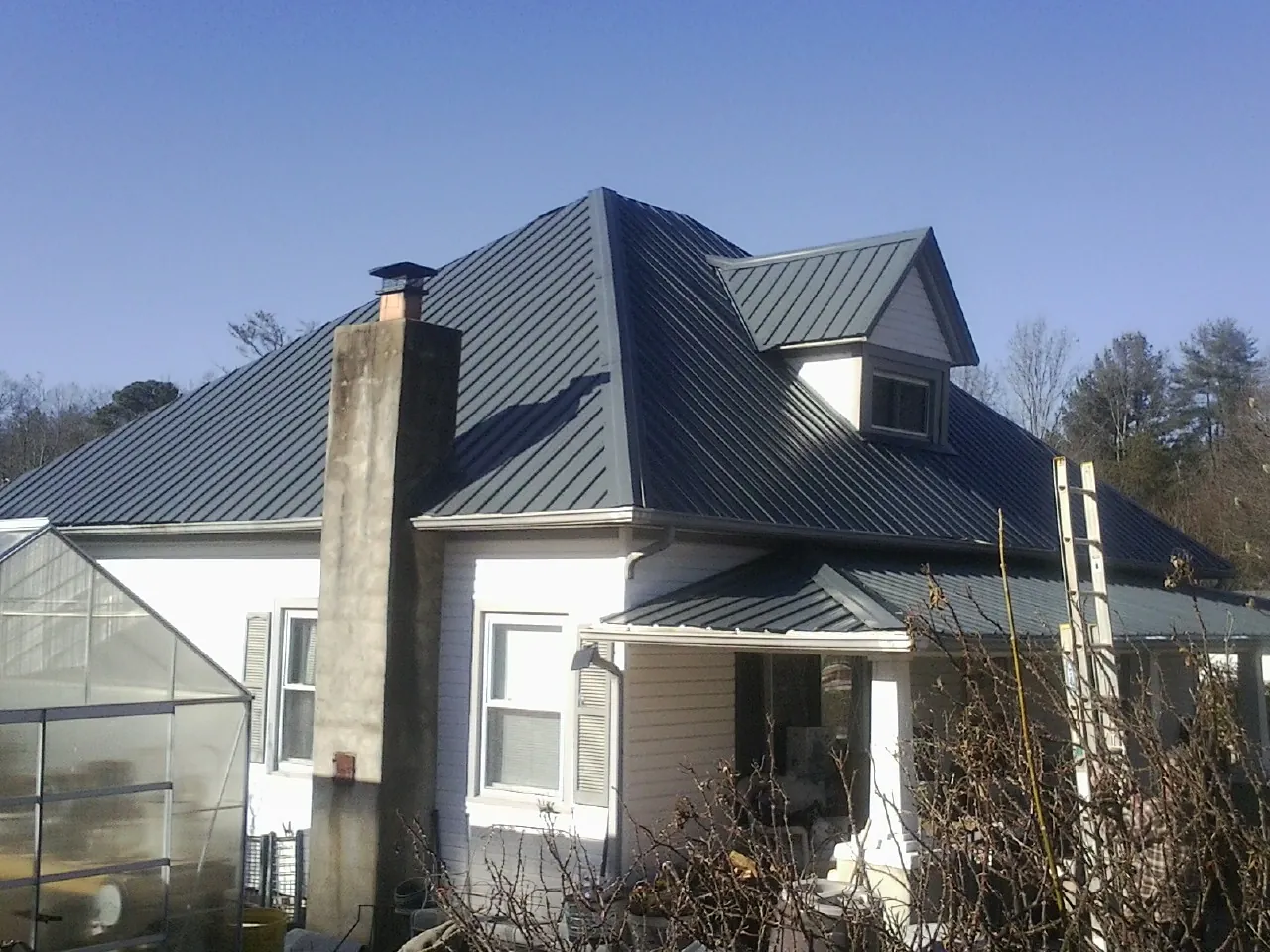 Dark blue standing seam metal roof on a white farmhouse with dormer — Slate & Tile Roof Repair by Roofing Brothers in Dateland