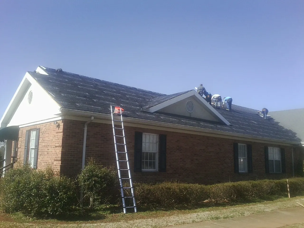 Crew tearing shingles off a brick ranch roof with a ladder set — Emergency Roof Repair work by our crew in Dateland