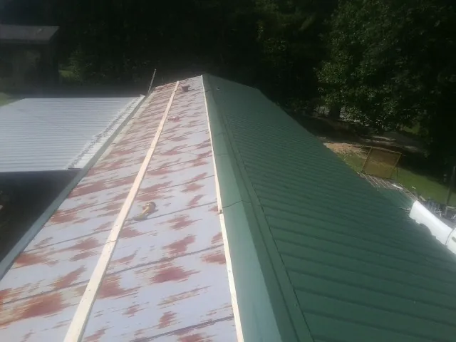Old rusted panels beside newly installed green metal roofing — Wind Damage Roof Repair by Roofing Brothers in Dateland