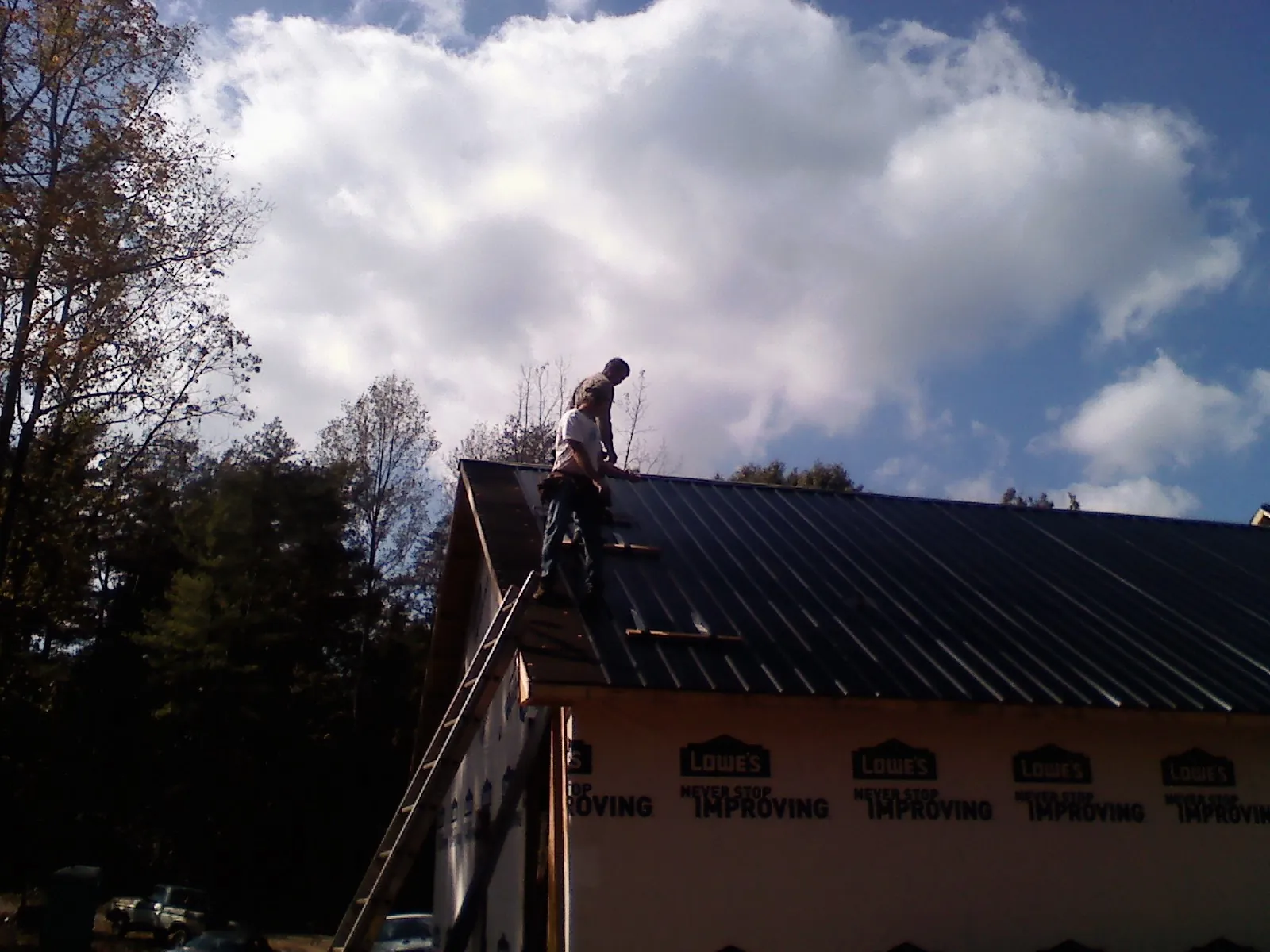 Roofer fastening dark metal panels high against a cloudy sky, from a Roof Inspection job in Dateland